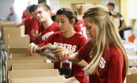 Three 侫Ƶ student wearing red "PIPERS" shirts taping cardboard boxes while volunteering