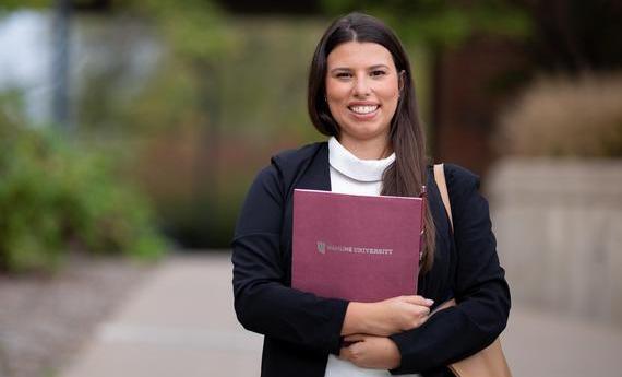 An MBA graduate student from 侫Ƶ's School of Business holding a folder and smiling at the camera