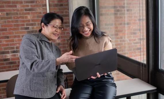A 侫Ƶ student and her advisor looking at a laptop together and smiling