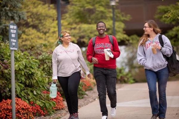 Three 侫Ƶ students walking and talking outside on campus in the fall