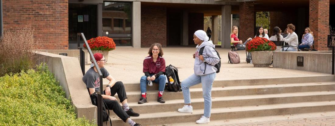 Three 侫Ƶ students gathered on a set of outdoor stairs on campus